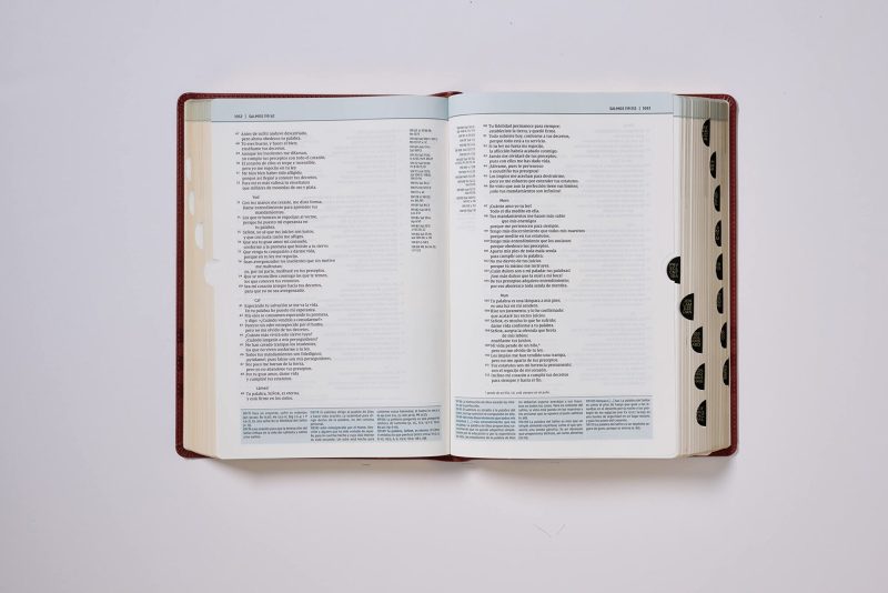 Un libro abierto con texto en español descansa sobre una superficie plana. Las páginas parecen ser de un libro de texto o religioso, resaltadas por pestañas adhesivas negras en el margen derecho que facilitan la navegación.