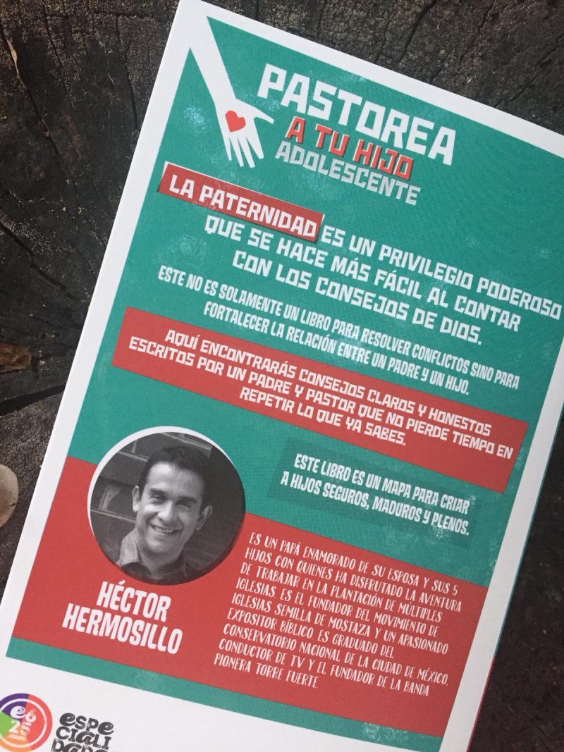 La imagen muestra un folleto con un diseño gráfico enfocado en la paternidad de adolescentes. En la parte superior, en un fondo rojo oscuro con letras blancas y verdes, destaca el título PASTOREA A TU HIJO ADOLESCENTE. La sección media del folleto tiene un fondo verde con texto en blanco y rojo que habla sobre la importancia de la paternidad y cómo el libro puede ayudar a mejorar la relación entre padres y adolescentes. En la parte inferior, aparece una foto circular de un hombre sonriente, identificado como Héctor Hermosillo, quien parece ser el autor o una figura relacionada con el contenido del folleto. El fondo de la imagen es texturizado, sugiriendo que el folleto está sobre una superficie con patrones de madera o material similar.