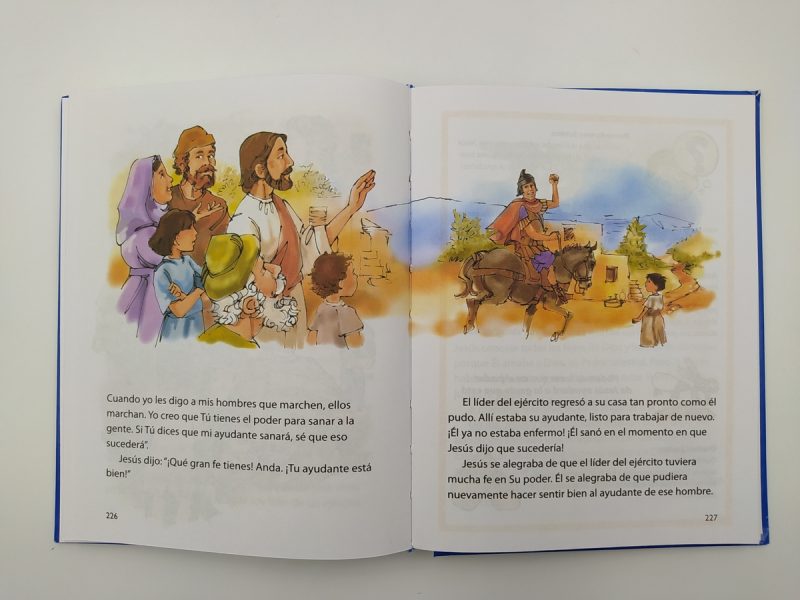 Página doble de un libro ilustrado abierto, mostrando dos escenas bíblicas. A la izquierda, Jesús y sus seguidores interactúan con una multitud, mientras que a la derecha un líder militar habla con un niño en un entorno antiguo.