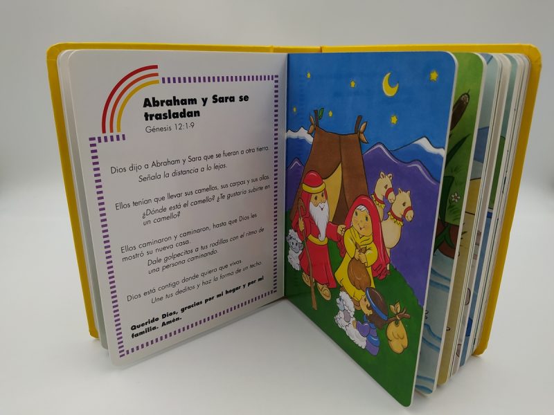 Libro infantil de tapas duras abierto en una página que describe la historia de 'Abraham y Sara se trasladan' junto a una ilustración colorida de Abraham, Sara y animales en un paisaje nocturno.