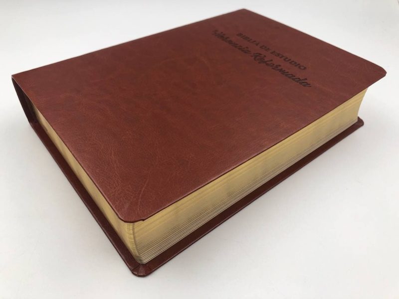 Libro con tapa de cuero marrón con bordes dorados y el títuloBIBLIA DE ESTUDIO inscrito en la parte superior, junto con un nombre personalizado impreso en la parte inferior.