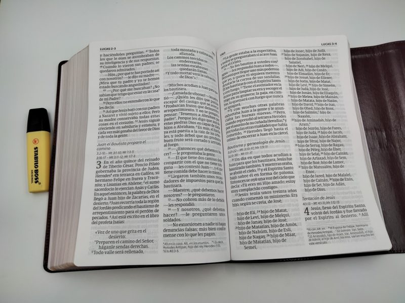 ** Libro abierto de la Biblia con un marcador amarillo al lado.