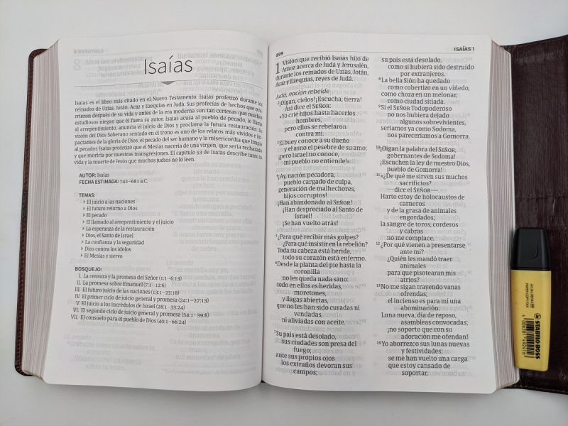** Una Biblia abierta en el Libro de Isaías con un resaltador amarillo junto a ella sobre una superficie blanca.