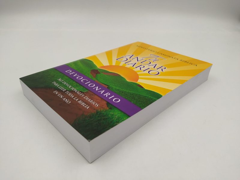 Libro titulado 'Devocionario Andar Diario' con un diseño de portada que muestra un paisaje soleado y una senda flanqueada por césped verde.