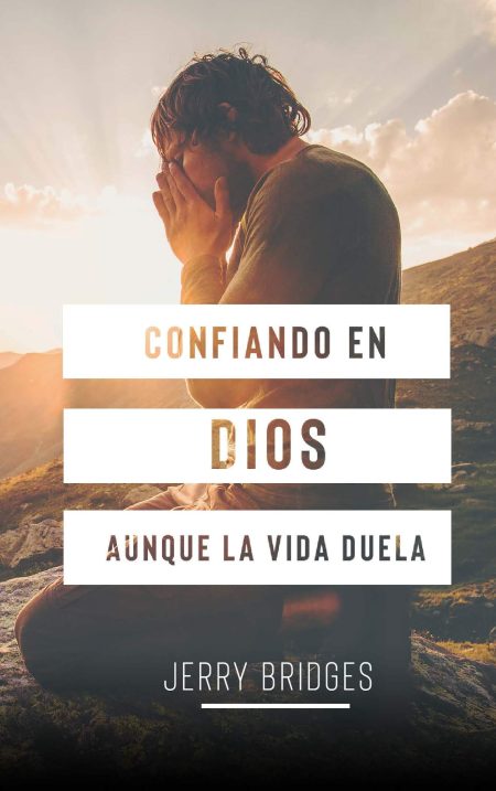 Imagen de un hombre rezando en la naturaleza con las manos juntas y rostro cubierto por ellas, en un entorno montañoso bajo un cielo iluminado por los rayos del sol al atardecer. Texto 'Confiando en Dios aún cuando la vida duele' y el nombre 'Jerry Bridges' en la parte inferior.