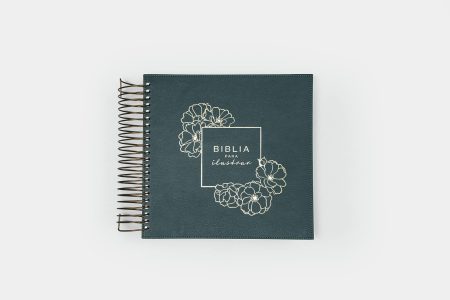 Cuaderno de tapa dura color azul oscuro con espiral y título 'Biblia para ilustrar' rodeado por un diseño de flores blancas sobre un fondo blanco.