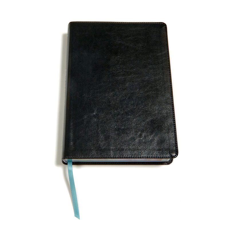 Una libreta negra cerrada con una cinta marcadora turquesa asomándose, sobre un fondo blanco.
