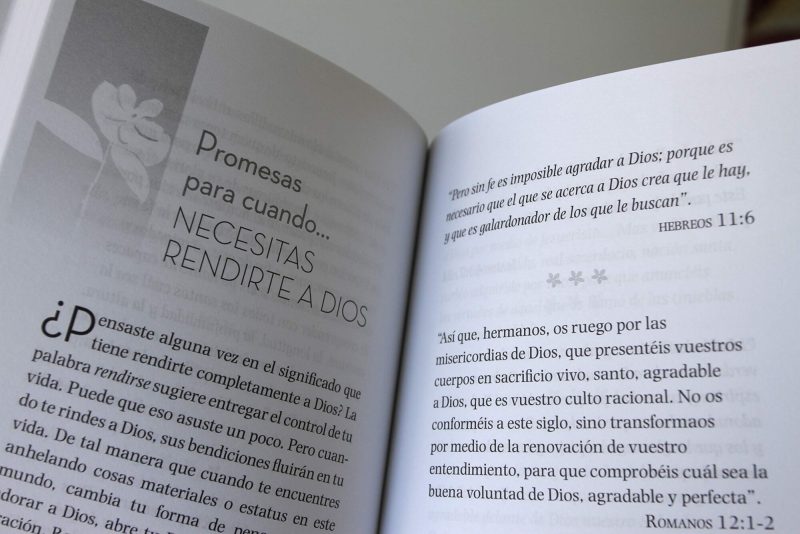 Fotografía de un libro abierto mostrando dos páginas con texto en español que incluyen títulos y citas bíblicas, con una decoración de flores discretas en gris.