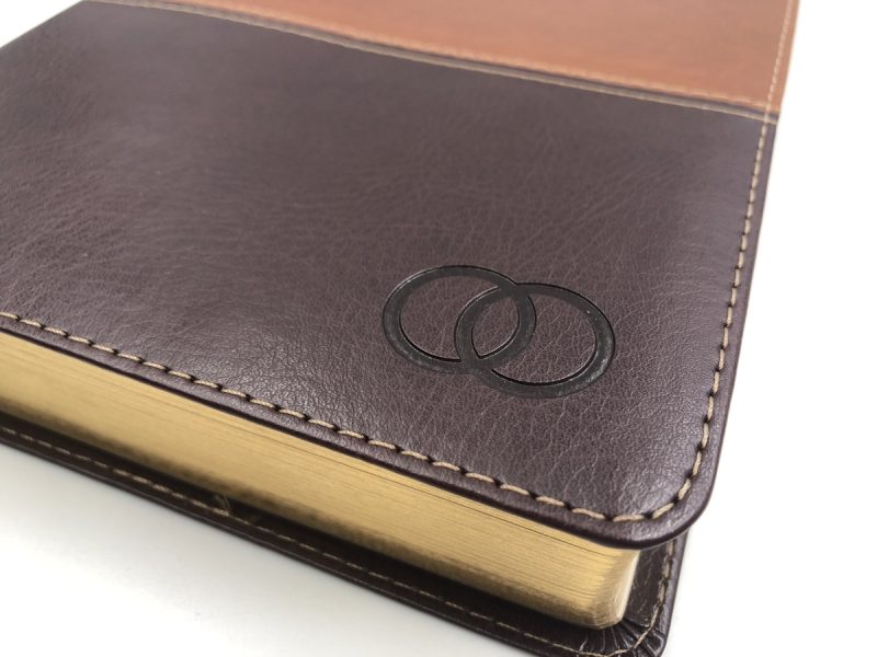 ** Primer plano de una Biblia con tapa de cuero marrón y un diseño de anillos entrelazados.