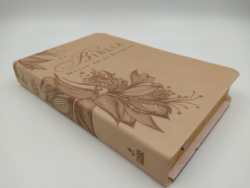 Una Biblia de tonos crema con una cubierta decorada con motivos florales y las palabras 'Biblia, Mujer en el espejo' en relieve.