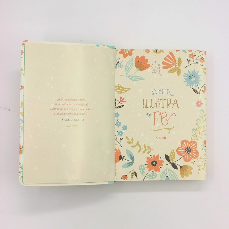 ** Un libro abierto con un diseño colorido de flores y hojas en la página derecha que dice "Ilustra tu Fe".