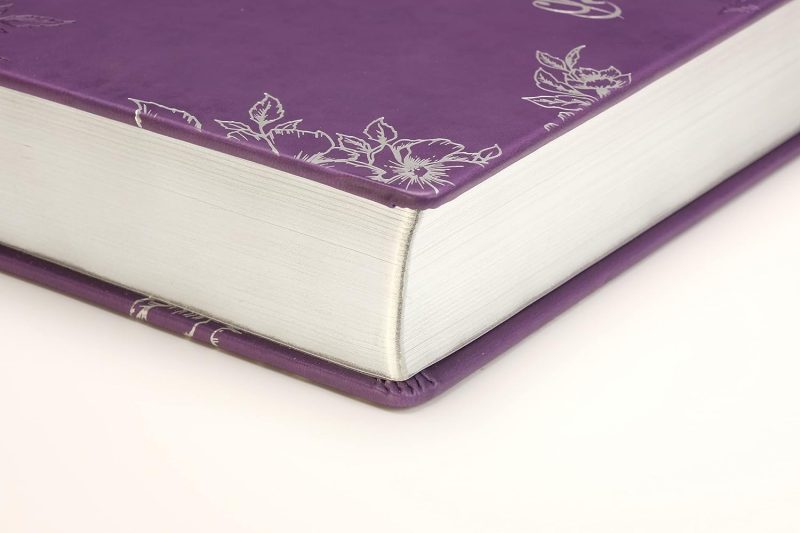 Primer plano de un libro con cubierta de cuero púrpura y detalles florales plateados.**