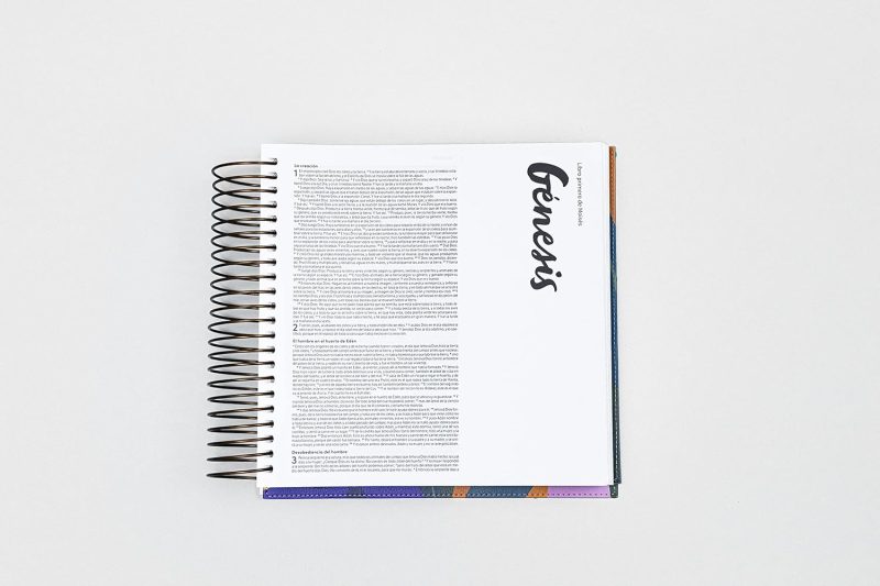 ** Vista cenital de un libro abierto mostrando una página con el texto "Génesis" y texto en columna a la izquierda.
