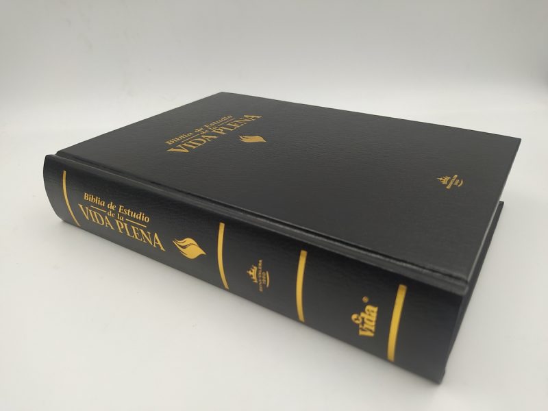 ** Biblia de Estudio Vida Plena con tapa dura negra y letras doradas sobre una superficie blanca.