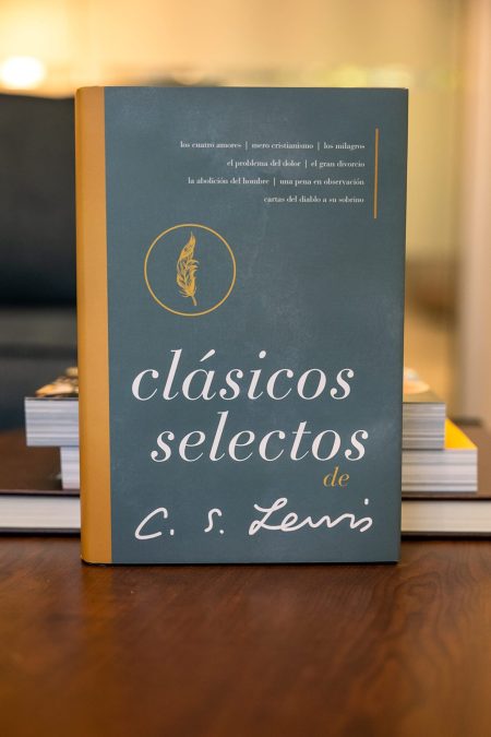 Un libro titulado 'clásicos selectos de C.S. Lewis' apoyado sobre una mesa de madera. La portada es de color azul verdoso con letras en blanco y dorado y un detalle circular que encierra una pluma de ave.