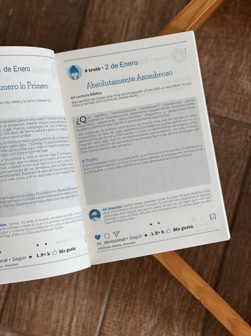 página de un libro o devocional que imita la estética de una publicación en redes sociales. La entrada del día, denominada Absolutamente Asombroso, cita un versículo bíblico de Isaías 469 y ofrece una reflexión y una oración relacionadas con el tema de reconocer la singularidad y el poder de Dios. Los elementos gráficos en la parte inferior simulan los de una plataforma de redes sociales, con iconos para 'me gusta', 'seguir', y un contador de reacciones. El libro está abierto sobre una superficie de madera y apoyado en un objeto de metal, como parte del marco de una silla o mesa, que entra en la imagen desde la parte inferior derecha.