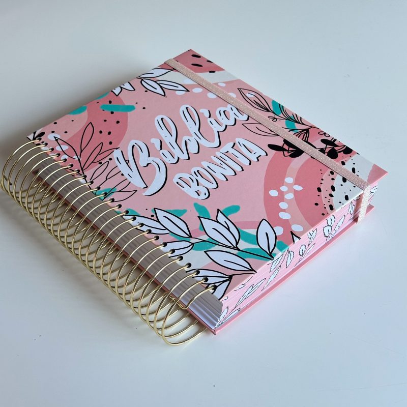 ** Biblia de cubierta rosa con diseño de flores y espiral dorado.