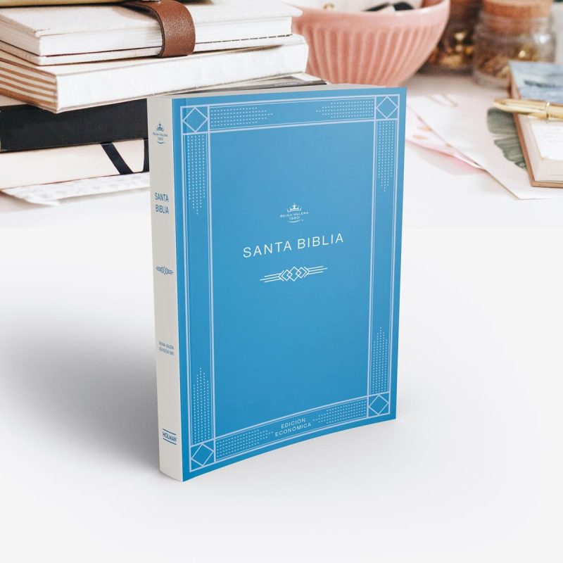 ** Una Biblia con cubierta azul claro colocada sobre una superficie blanca. Al fondo, se pueden ver otros libros y objetos de papelería.