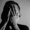En un retrato monocromo, un hombre se cubre la mitad del rostro con la mano en un gesto de reflexión o preocupación.