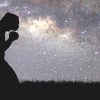 Silueta de una persona arrodillada en posición de oración o meditación sobre un fondo de cielo estrellado con la Vía Láctea.