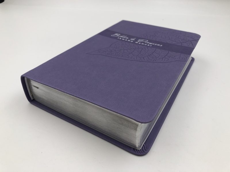 ** Libro de tapa dura con cubierta azul púrpura, visto en ángulo lateral sobre un fondo blanco.