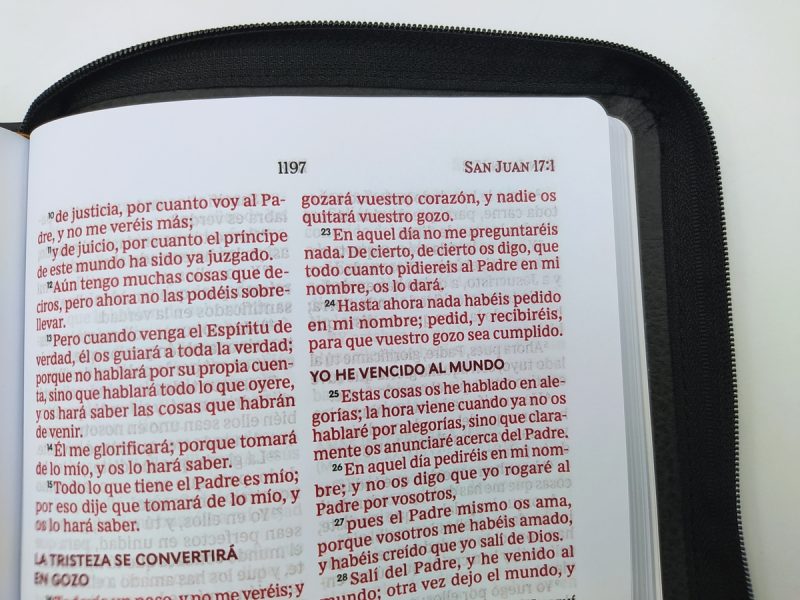 ** Página de la Biblia abierta con texto en el Evangelio de San Juan, capítulo 16, versos resaltados en rojo.
