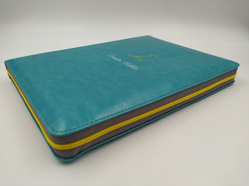 ** Vista en ángulo de un cuaderno con cubierta turquesa y bordes amarillos.