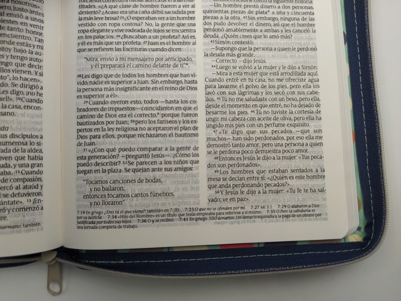 ** Primer plano de las páginas abiertas de un libro, con texto en columnas. El libro está guardado en un bolso con cremallera visible en el borde derecho.