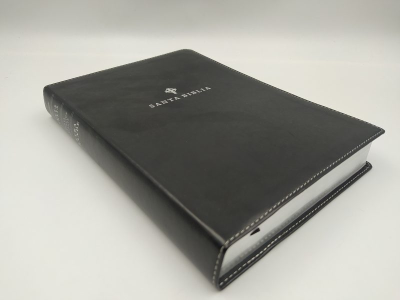 ** Una Biblia con tapa negra, cerrada y mostrando parte del lomo, sobre una superficie blanca.