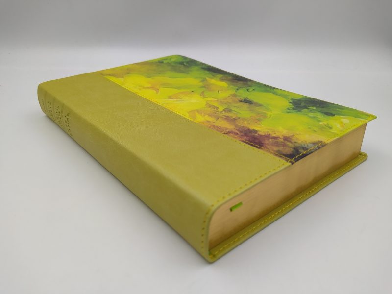 ** Libro cerrado con una cubierta de cuero verde y un diseño abstracto en tonos amarillos y verdes en la parte superior.