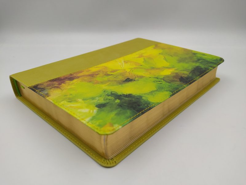 ** Un libro de tapa dura con un diseño artístico en tonos verdes y amarillos, colocado sobre una superficie blanca.