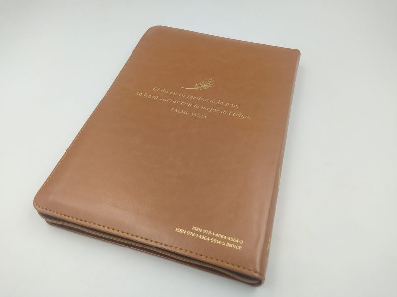 ** Una Biblia con cubierta de cuero marrón claro está colocada sobre una superficie blanca. En la portada se pueden ver letras doradas que forman una inscripción.