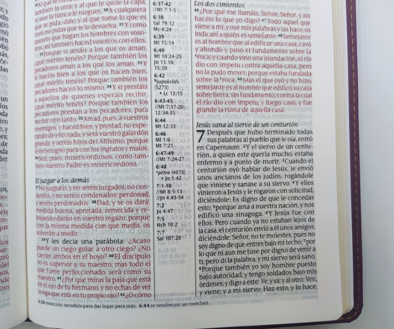 ** Página abierta de una Biblia con texto en rojo y negro. Se presentan columnas de texto con referencias y palabras resaltadas.