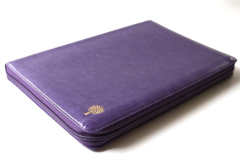 ** Funda violeta de cuero cerrada con un pequeño emblema dorado en una esquina.