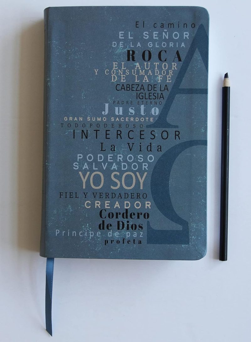** Cuaderno azul con palabras religiosas grabadas y un lápiz negro al lado.