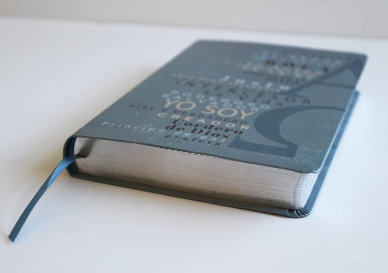 ** Una Biblia cerrada con una cubierta azul y una cinta marcadora en una mesa blanca.