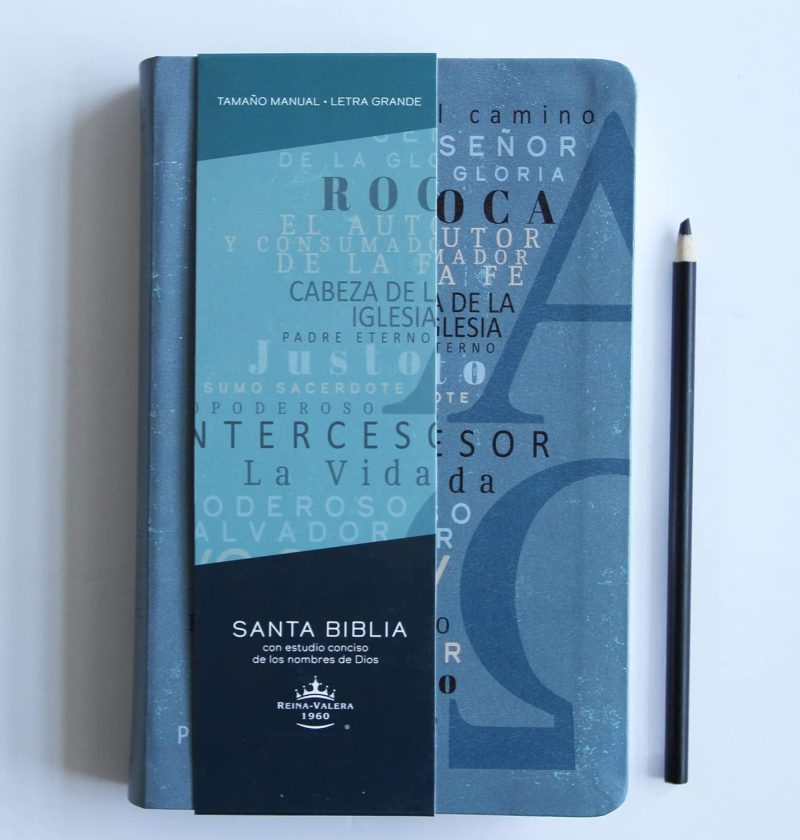** Biblia de tapa dura azul con diseño tipográfico y lápiz negro al lado.