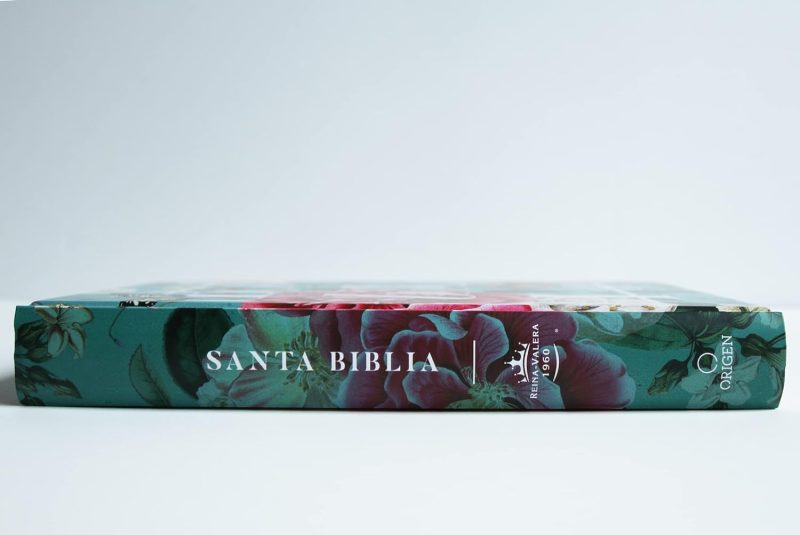 ** Vista lateral de una Biblia con tapa de diseño floral sobre un fondo blanco.
