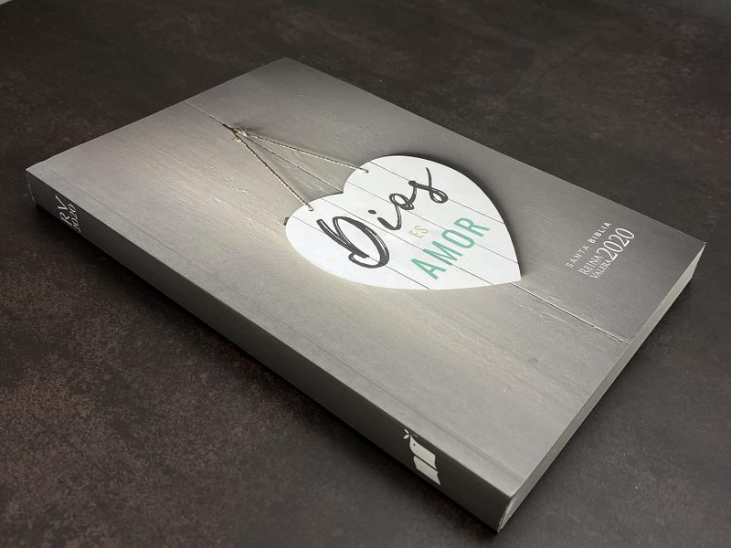 ** Un libro titulado "Dios es Amor" con un diseño de portada gris y un corazón blanco en el centro, colocado sobre una superficie oscura.