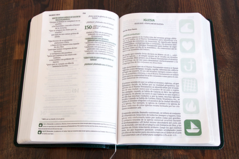 ** Una Biblia abierta sobre una mesa de madera, mostrando texto en español y diferentes iconos en el borde de las páginas.