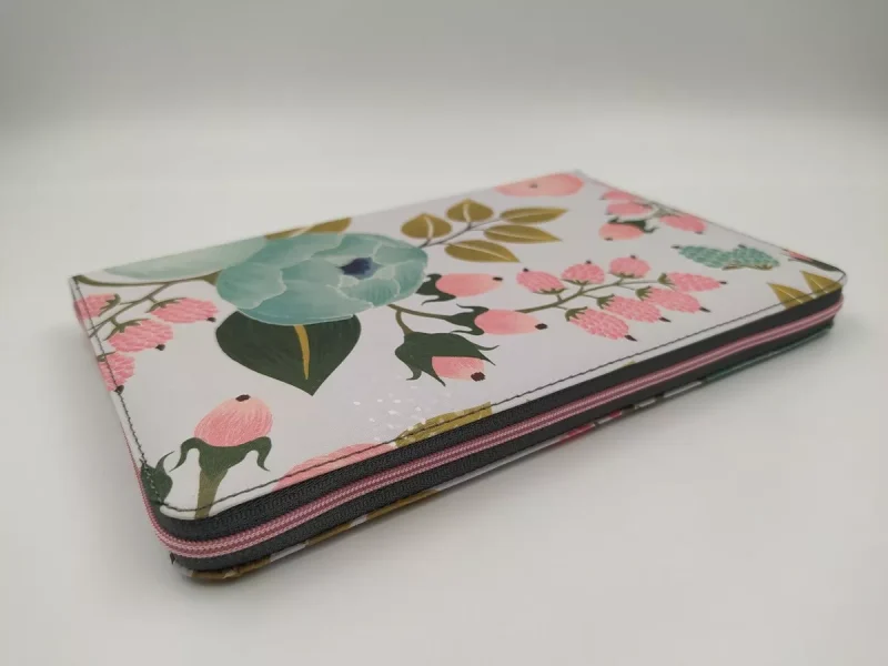 ** Estuche plano con diseño de flores y hojas en tonos verdes, rosados y azules, con una cremallera alrededor.