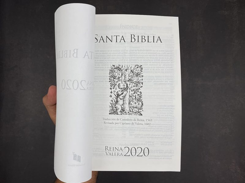 ** Una mano sosteniendo una página de la Santa Biblia, edición Reina-Valera 2020.