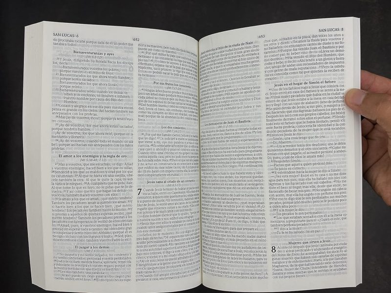 ** Una mano sostiene una Biblia abierta mostrando texto en columnas.