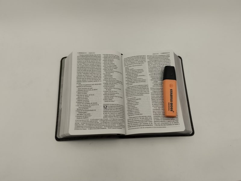 ** Una Biblia abierta con un resaltador naranja encima.