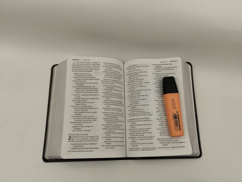 ** Una Biblia abierta con un marcador resaltador naranja sobre sus páginas.