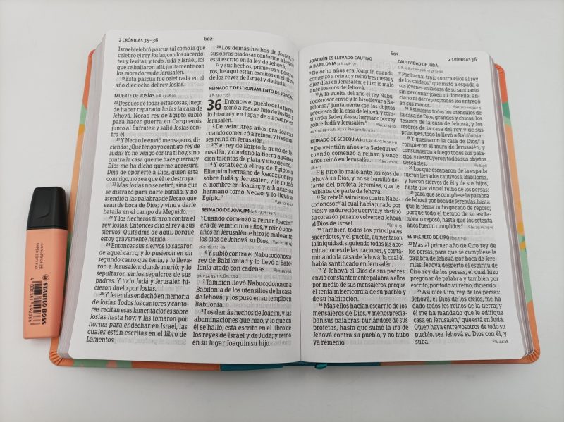 ** Biblia abierta junto a un marcador naranja sobre una superficie blanca.