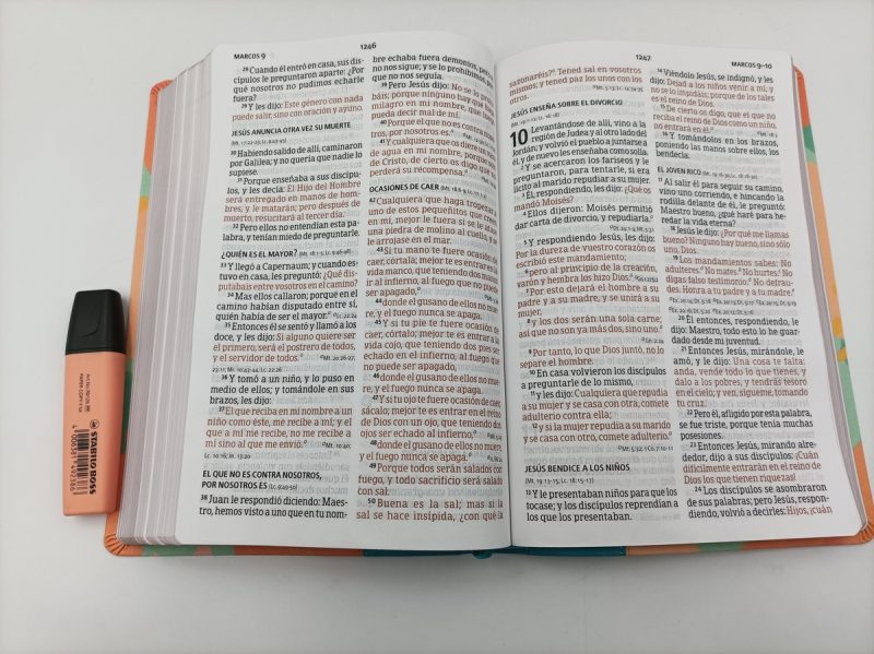 ** Biblia abierta junto a un resaltador naranja sobre una mesa blanca.
