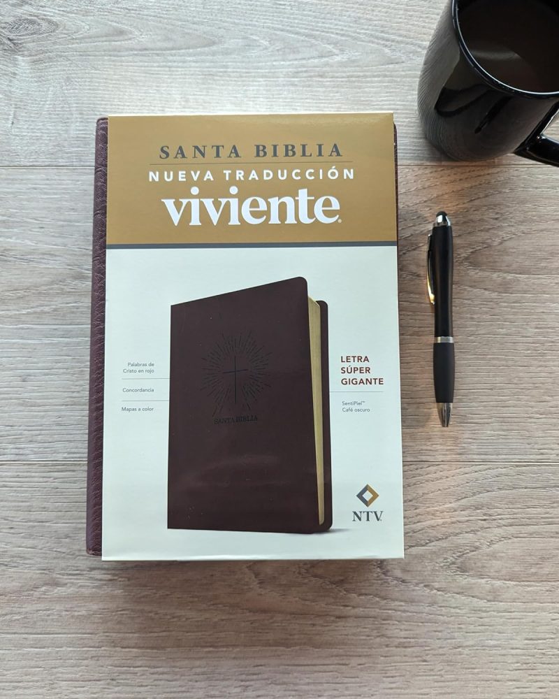 ** Biblia Nueva Traducción Viviente sobre una mesa con una taza de café y un bolígrafo negro.