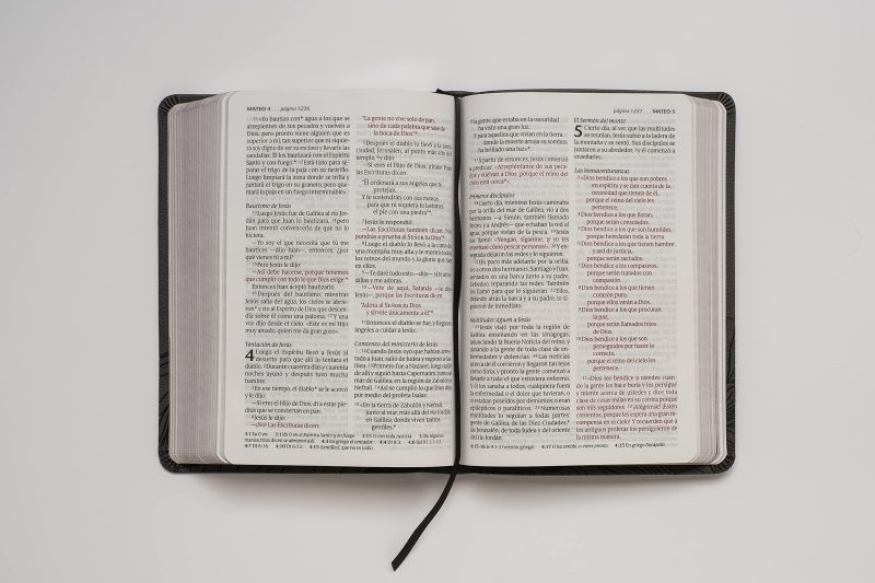 ** Biblia abierta sobre una superficie blanca, mostrando texto en dos columnas.