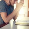 Hombre joven orando con una Biblia abierta frente a él en una mesa